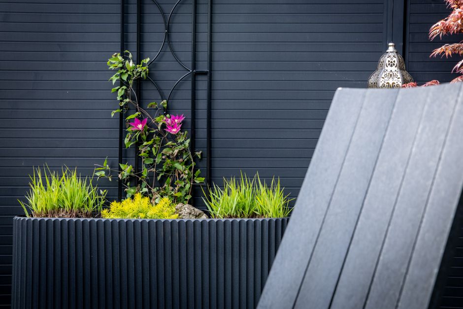 Rechthoekige cortenstaal plantenbakken op een modern terras met groene planten en bloemen.